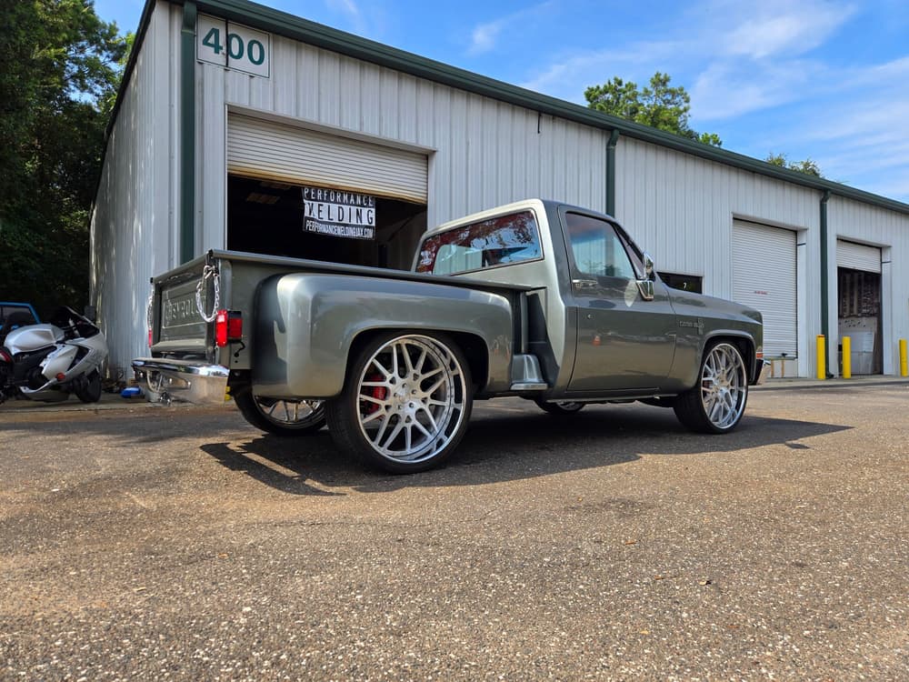 A lowered gray squarebody Chevy C10 on billet wheels parked outside the shop.