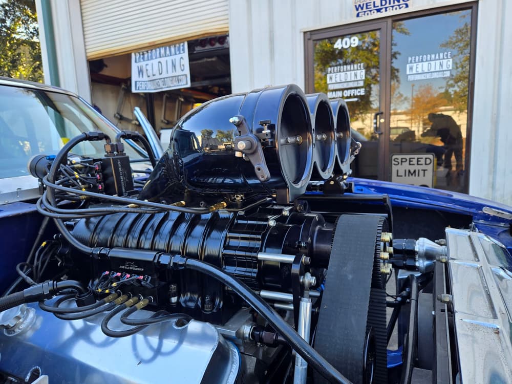 Supercharged race engine with twin throttle bodies and fabricated chassis outside the shop.