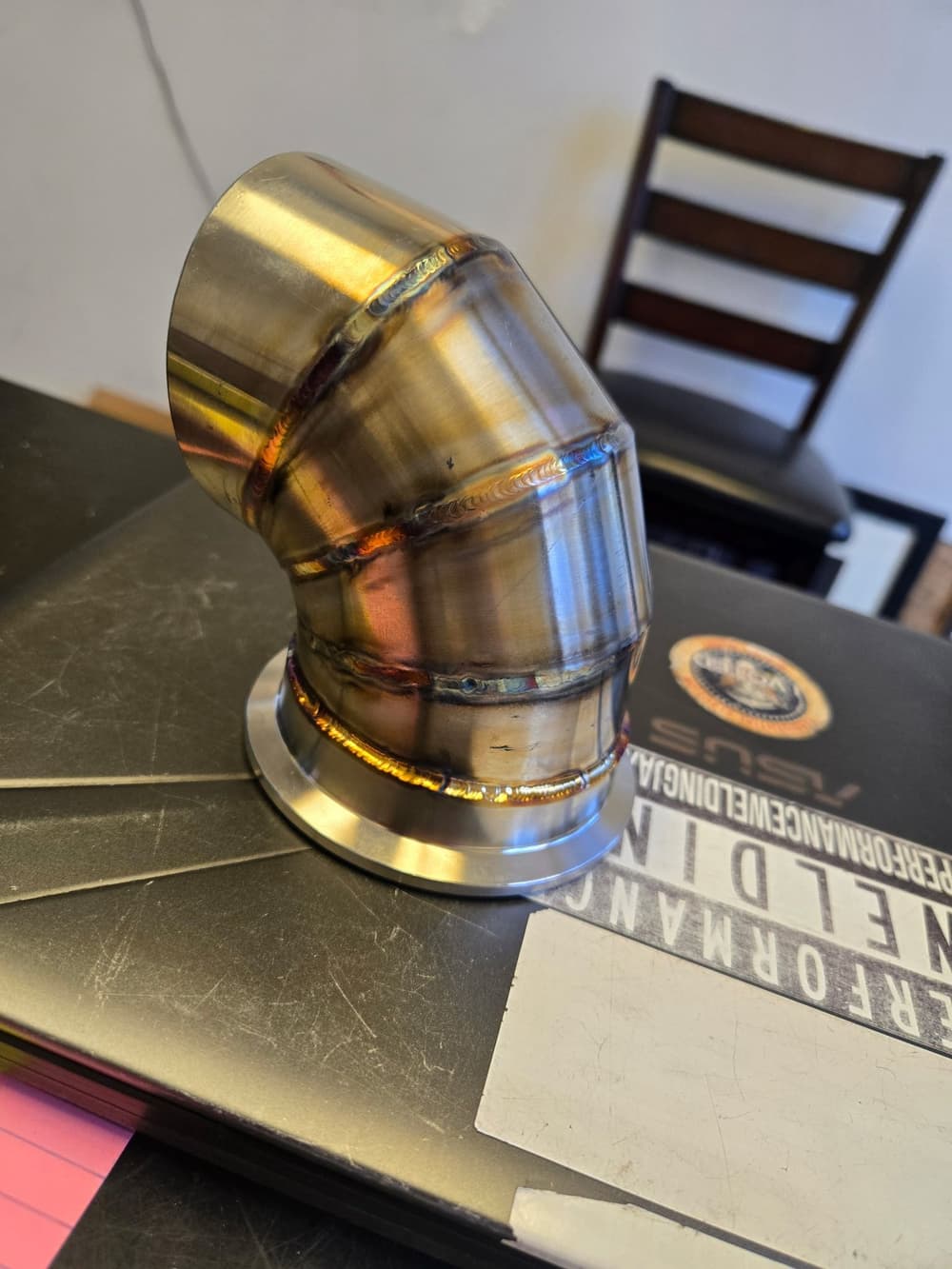 Close-up of a fabricated stainless pipe elbow with rainbow heat-tinted TIG weld beads.
